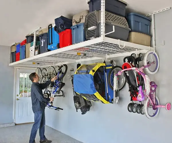 Overhead garage storage rack holding bins, with bikes and gear hung on the wall below